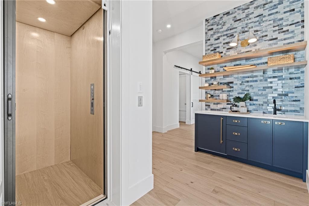 Bar area with a barn door, elevator, open shelves, light wood-style floors, and recessed lighting