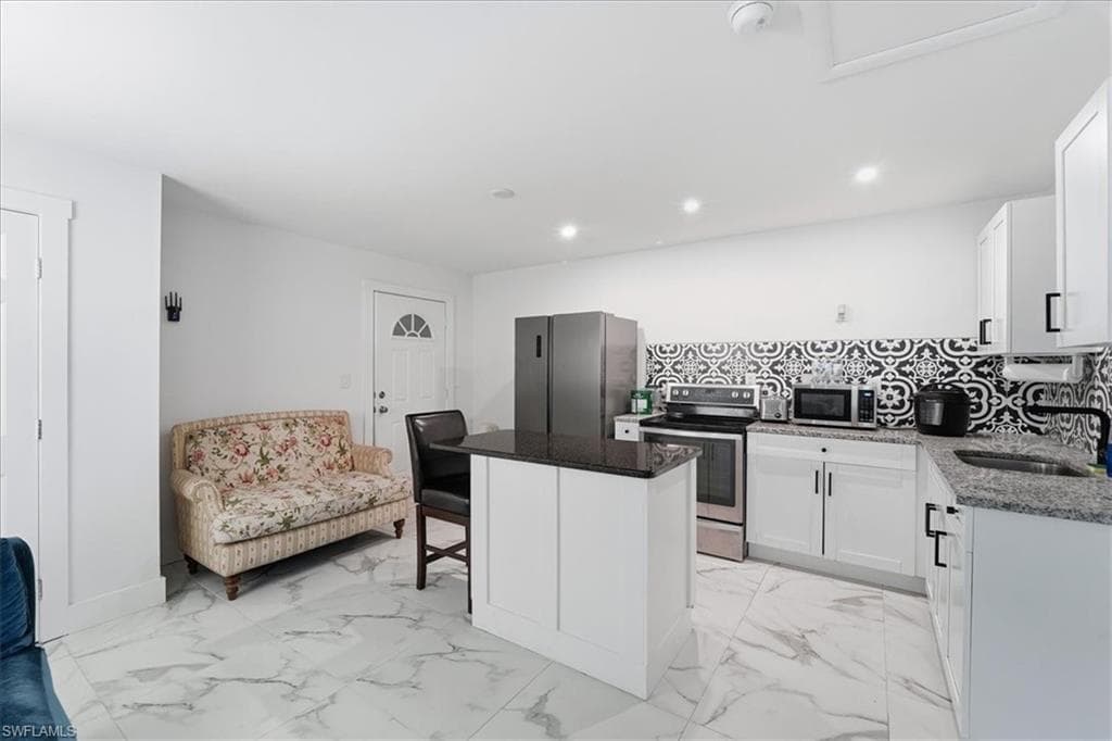 Kitchen with a breakfast bar, dark stone countertops, light marble finish floors, appliances with stainless steel finishes, and white cabinets