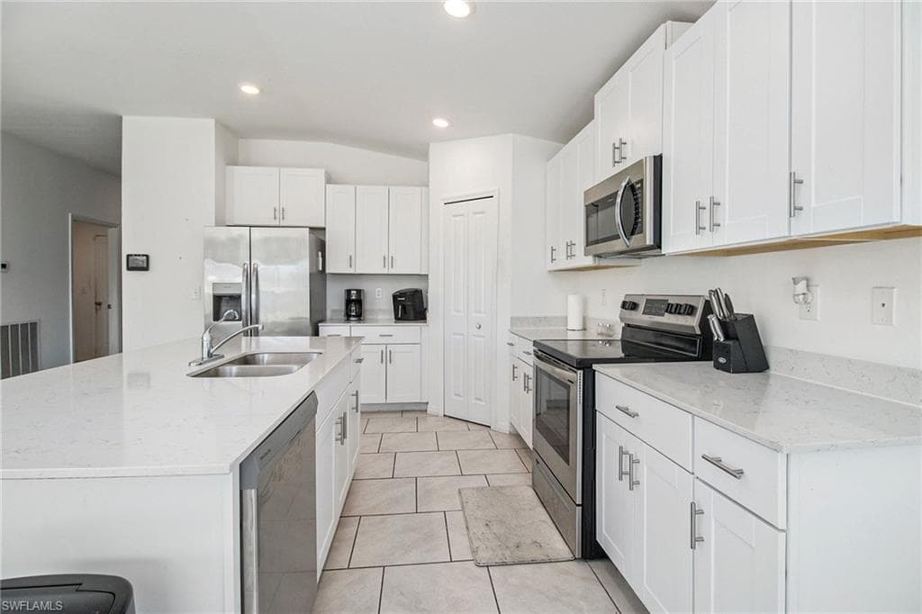Kitchen with appliances with stainless steel finishes, a center island with sink, white cabinets, light stone countertops, and light tile patterned floors