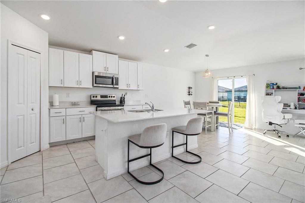 Kitchen with white cabinetry, appliances with stainless steel finishes, a breakfast bar, decorative light fixtures, and recessed lighting