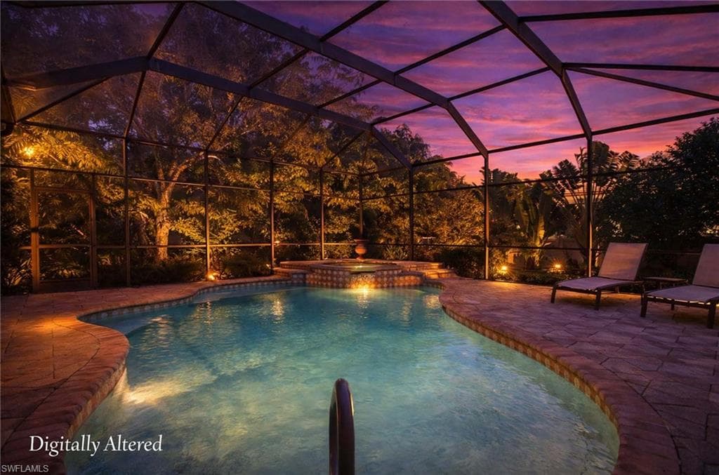 Pool at dusk featuring glass enclosure, a pool with connected hot tub, and a patio area