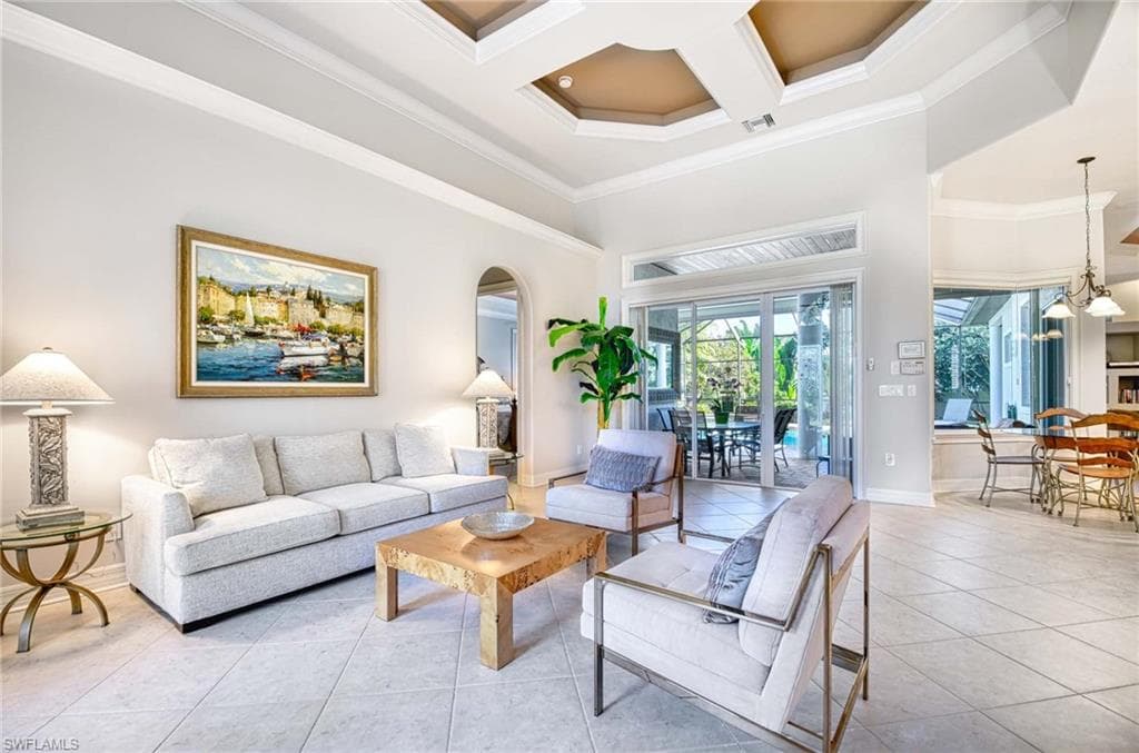 Living room with a towering ceiling, light tile patterned floors, coffered ceiling, crown molding, and a chandelier