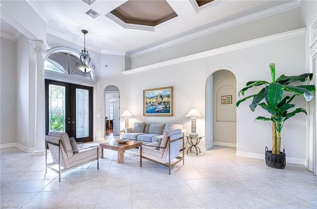 Living area with a high ceiling, arched walkways, french doors, ornamental molding, and coffered ceiling