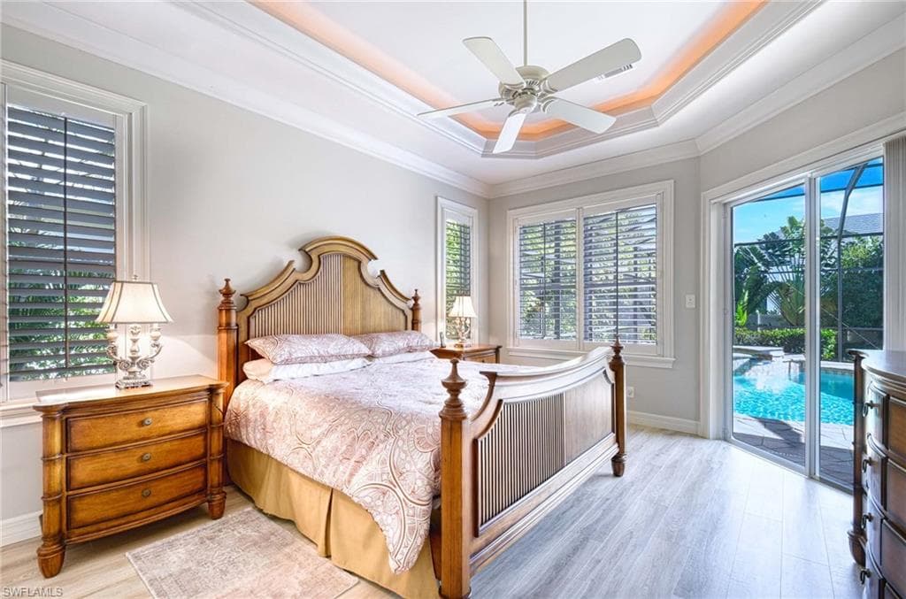 Bedroom featuring wood finished floors, a tray ceiling, access to exterior, ceiling fan, and crown molding