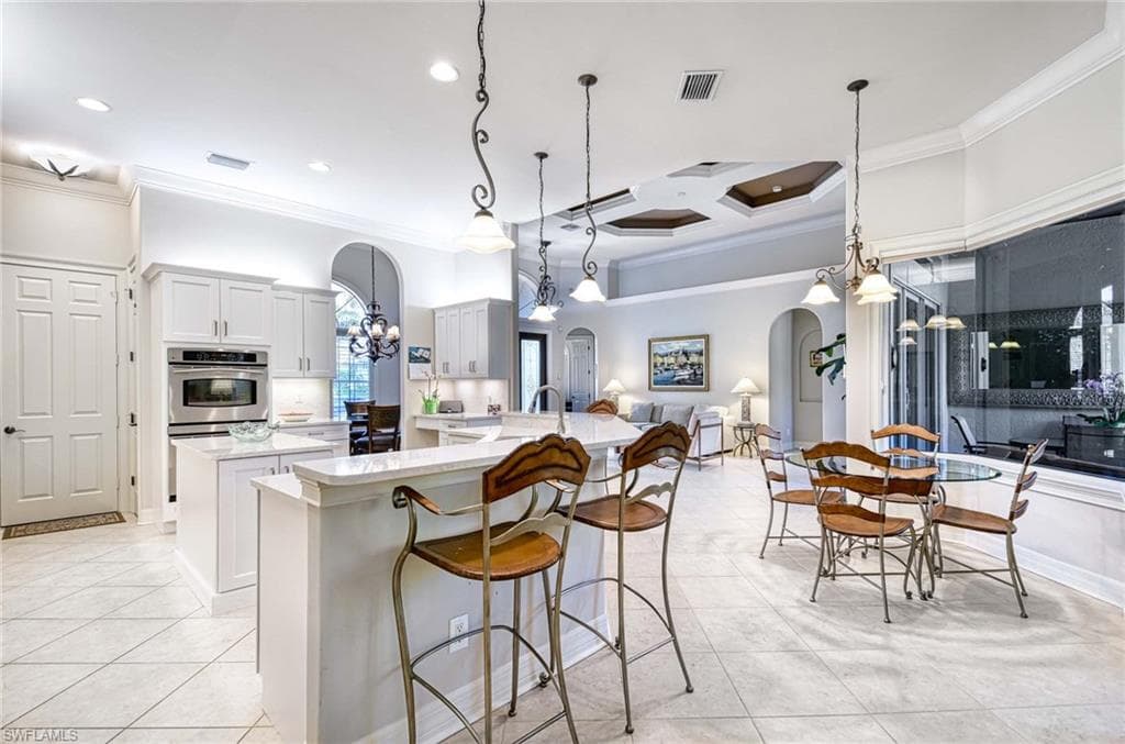 Kitchen with arched walkways, a chandelier, coffered ceiling, ornamental molding, and decorative light fixtures
