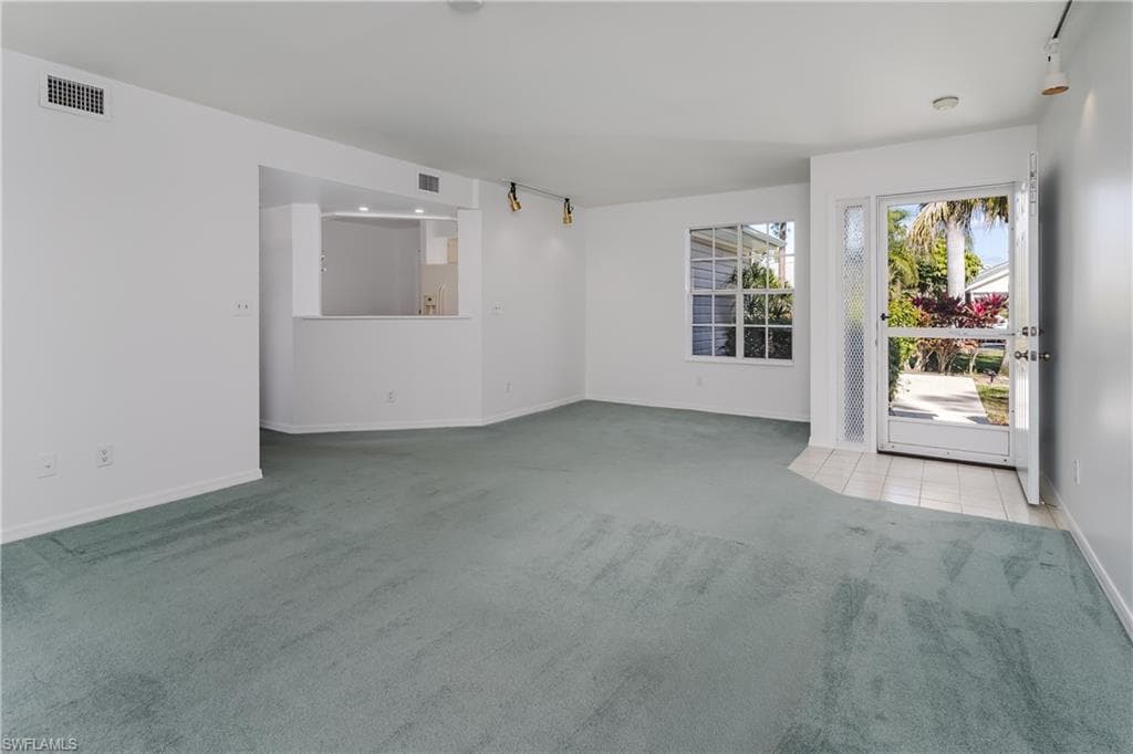 Unfurnished living room featuring track lighting and light carpet