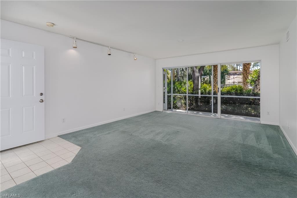 Carpeted empty room featuring track lighting and tile patterned flooring