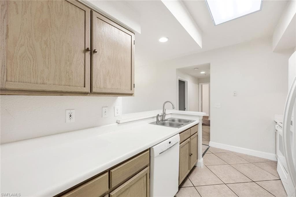 Kitchen featuring light countertops, light brown cabinetry, white appliances, and light tile patterned floors