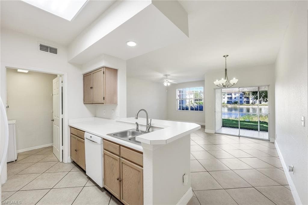 Kitchen with light brown cabinets, white countertops, open floor plan, light tile patterned flooring, and white appliances.