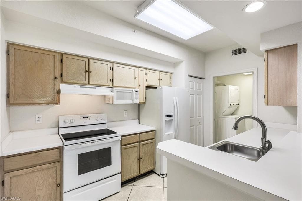 Kitchen with white appliances, light countertops and light brown cabinetry. Notice the Laundry Room in the background