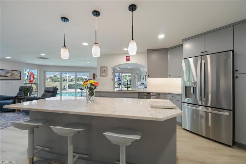 Kitchen with gray cabinets, stainless steel appliances, open floor plan, a kitchen breakfast bar, and hanging light fixtures