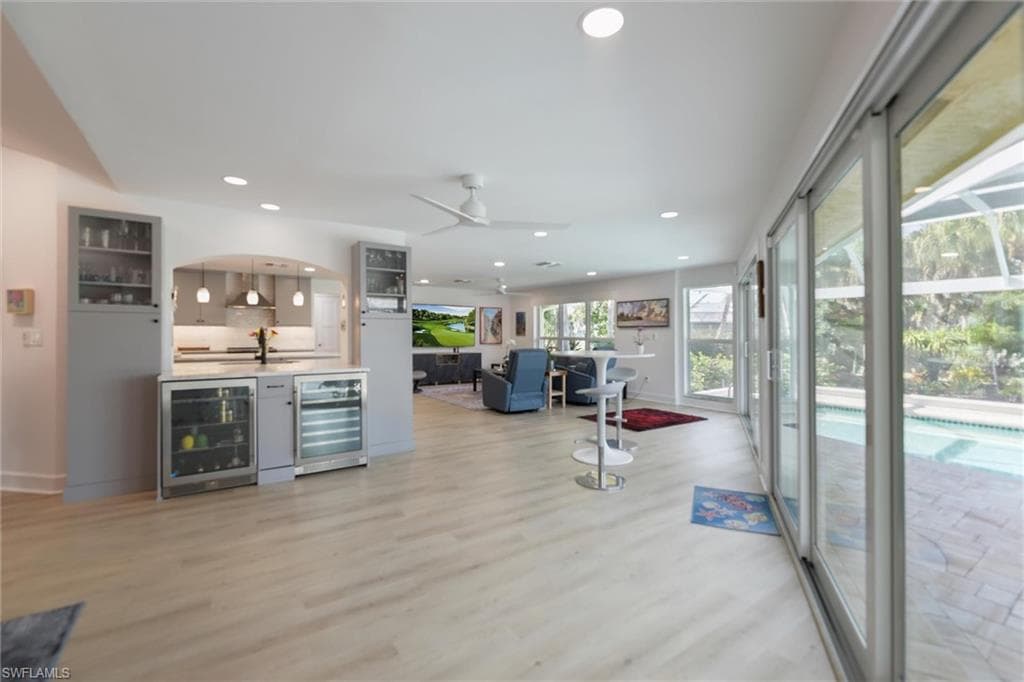 Indoor bar with glass insert cabinets, beverage cooler, gray cabinets, light wood-style flooring, and recessed lighting