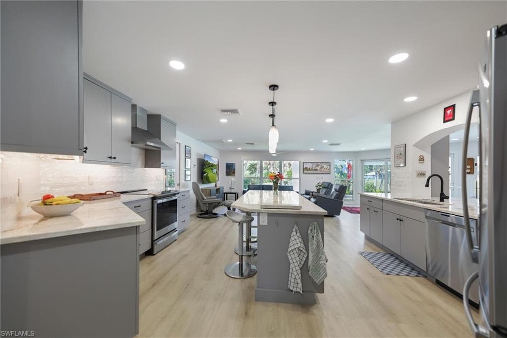 Kitchen with gray cabinetry, backsplash, decorative light fixtures, stainless steel appliances, and open floor plan