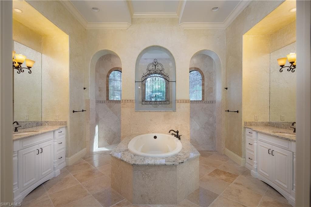Bathroom with a bath, a chandelier, ornamental molding, two vanities, and walk in shower