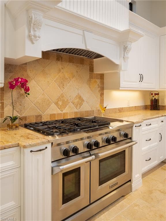 Kitchen featuring double oven range, white cabinets, and light stone counters