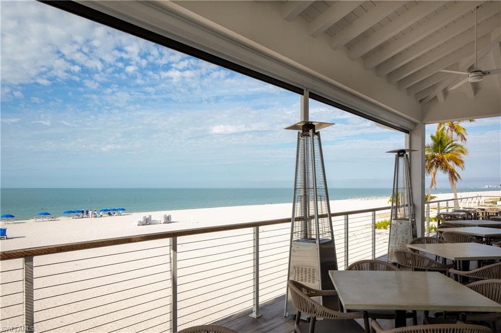 Balcony featuring view of water and beach, outdoor dining area, and ceiling fan