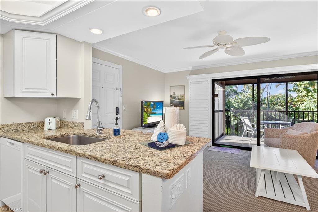 Kitchen featuring ornamental molding, light stone countertops, dishwasher, white cabinets, and a peninsula