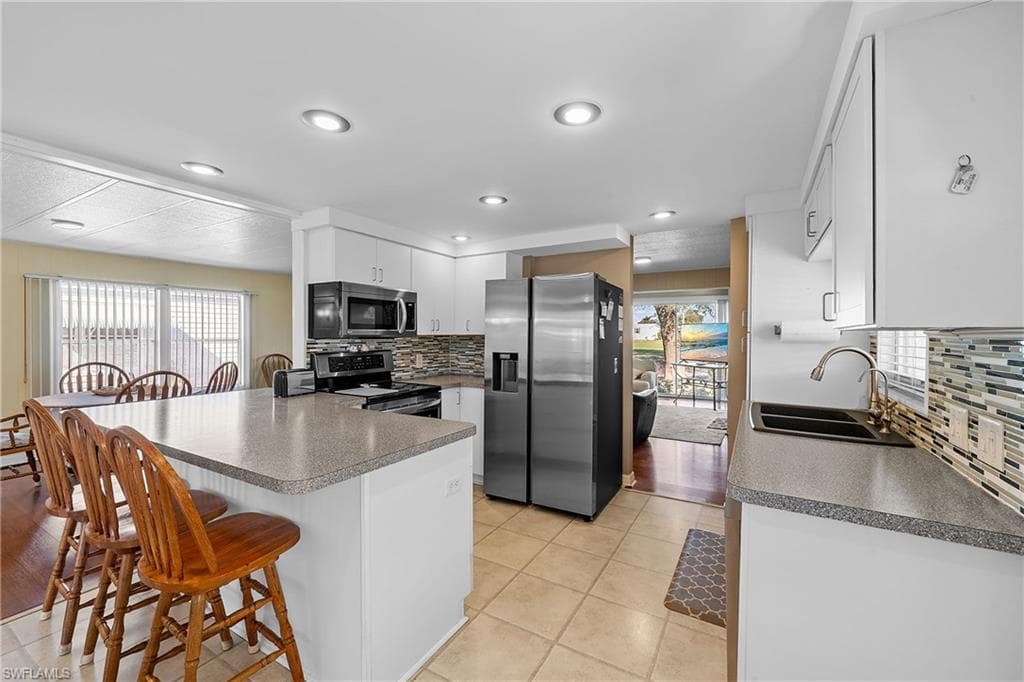 Kitchen with appliances with stainless steel finishes, backsplash, a peninsula, a breakfast bar area, and white cabinets