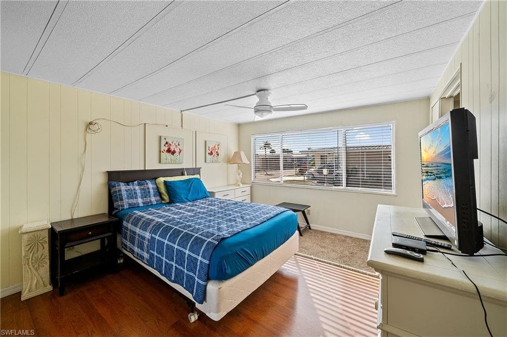 Bedroom with wood walls, wood finished floors, a ceiling fan, and a textured ceiling