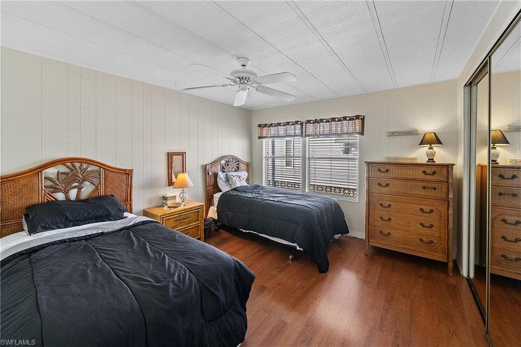 Bedroom with dark wood finished floors, a closet, ceiling fan, and wood walls