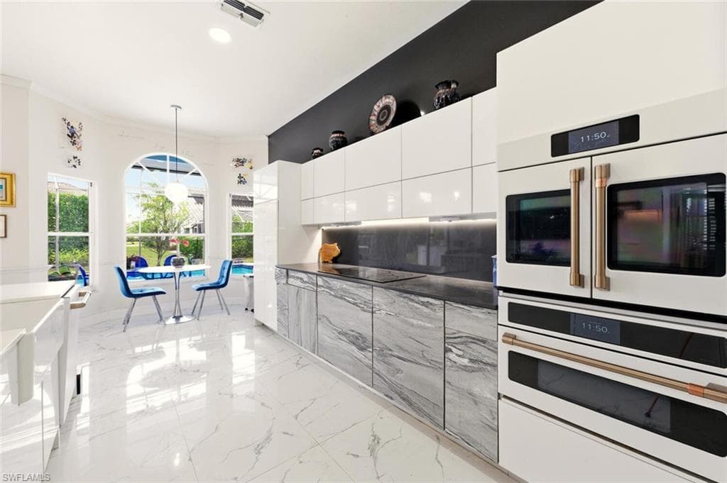 Kitchen featuring dark countertops, modern cabinets, pendant lighting, white double oven, and light marble finish flooring