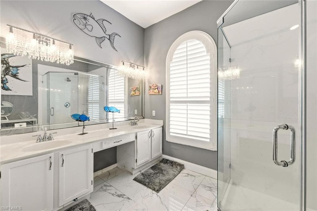 Bathroom with a marble finish shower, double vanity, and light marble finish flooring