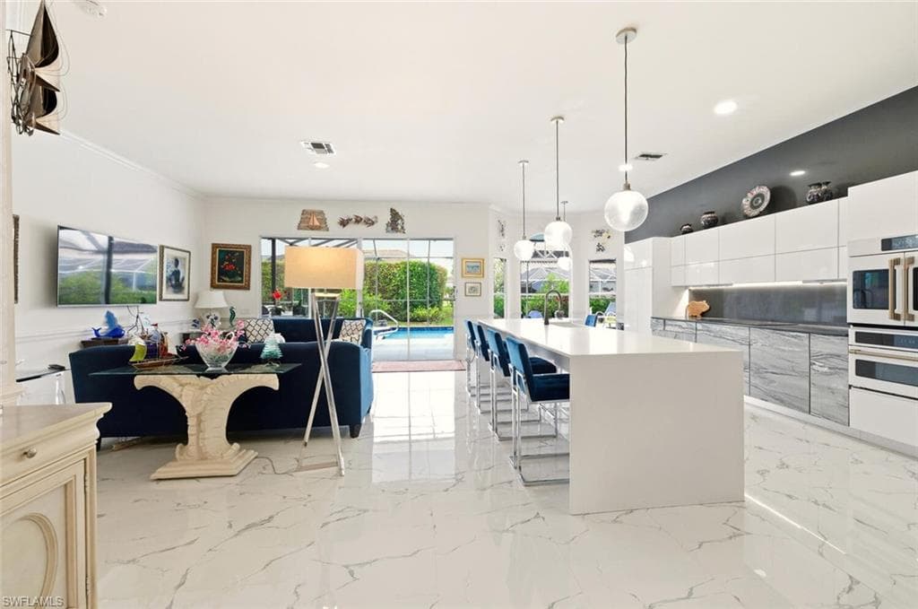 Kitchen with open floor plan, a kitchen island with sink, hanging light fixtures, modern cabinets, and a kitchen breakfast bar