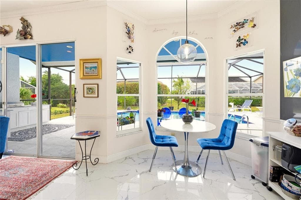 Dining area with a sunroom, ornamental molding, light marble finish floors, and healthy amount of natural light