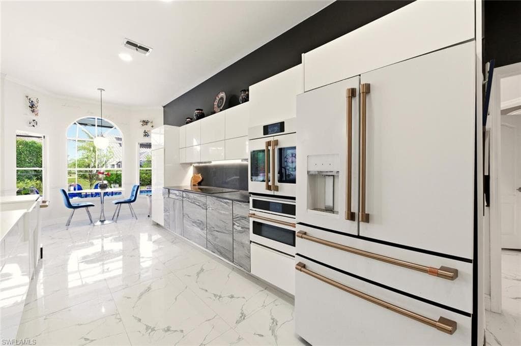 Kitchen featuring white appliances, decorative light fixtures, modern cabinets, light marble finish floors, and white cabinetry