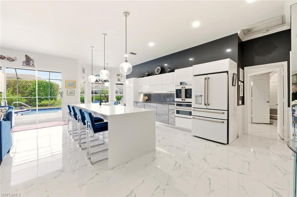 Kitchen featuring modern cabinets, white cabinets, white appliances, an island with sink, and a kitchen bar