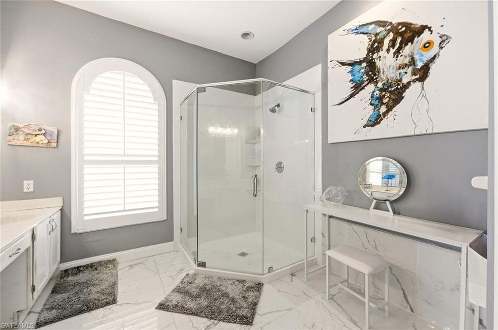 Full bathroom with vanity, a shower stall, plenty of natural light, and light marble finish floors