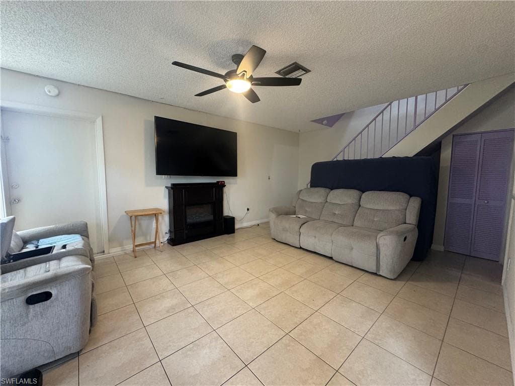 Living area featuring a fireplace, a textured ceiling, stairway, ceiling fan, and light tile patterned flooring