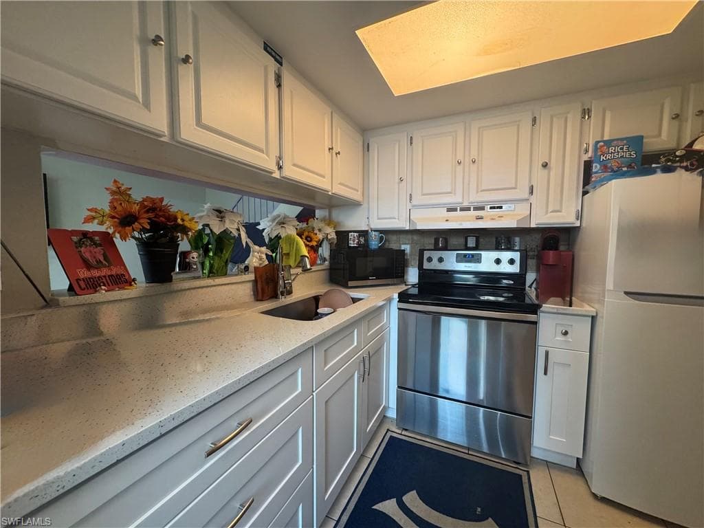 Kitchen featuring electric stove, freestanding refrigerator, white cabinetry, and light stone countertops