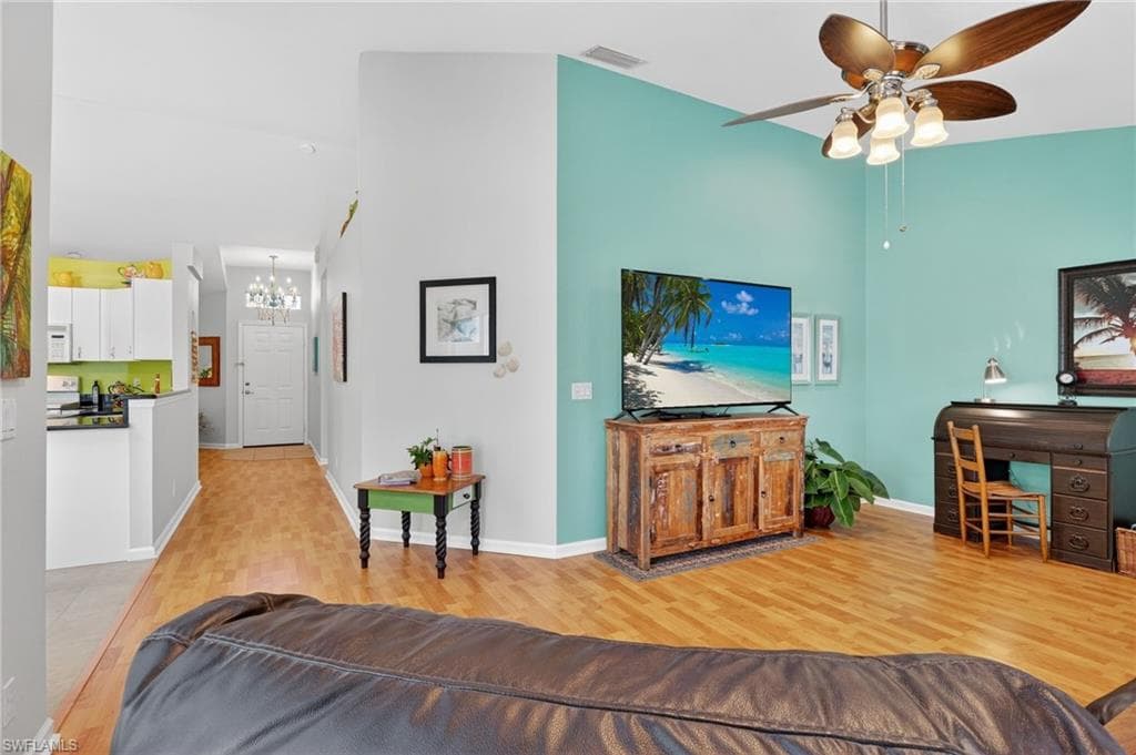 Living area featuring a towering ceiling, light wood-style floors, ceiling fan, and a chandelier