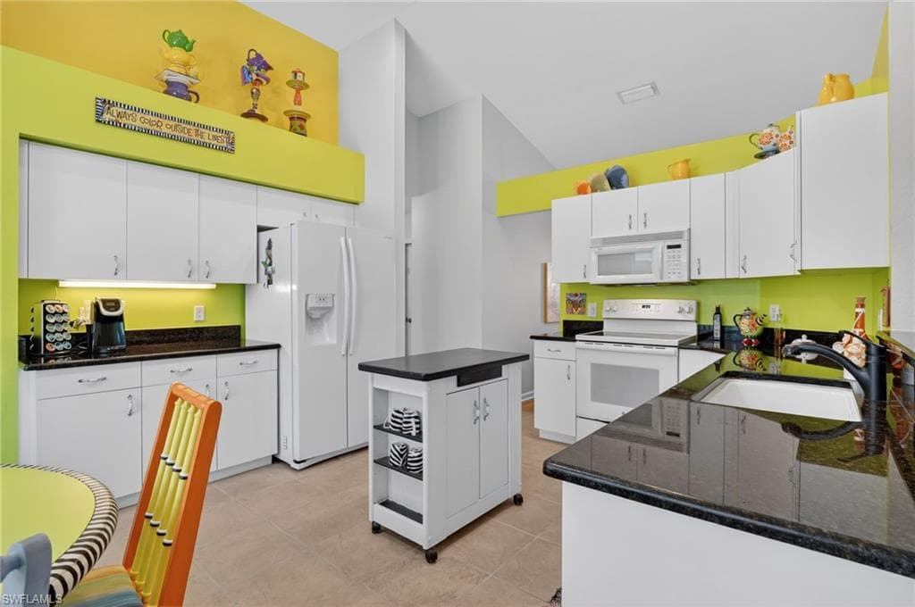 Kitchen with white appliances, white cabinets, dark stone counters, and a kitchen island