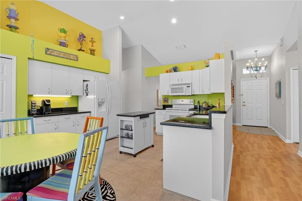 Kitchen with white appliances, a high ceiling, white cabinetry, a peninsula, and a chandelier