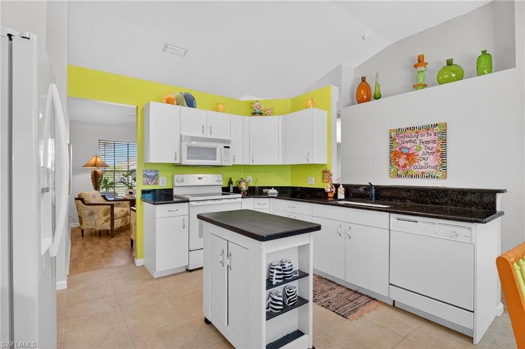Kitchen with white appliances, white cabinetry, light tile patterned flooring, lofted ceiling, and a kitchen island