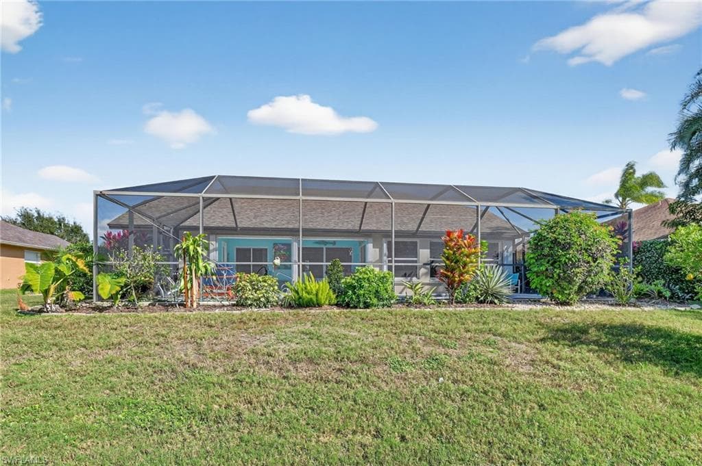 Rear view of property with glass enclosure, a lawn, and a sunroom