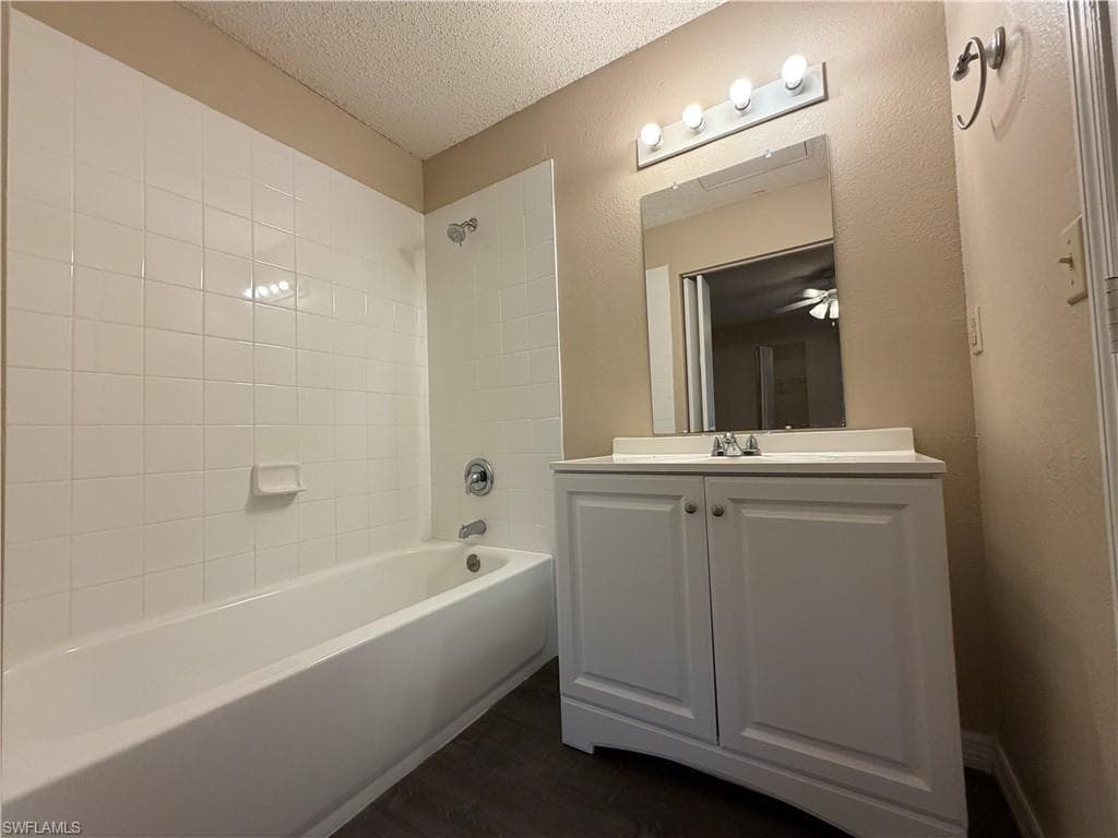 Full bathroom with vanity, washtub / shower combination, a textured ceiling, dark wood finished floors, and a textured wall
