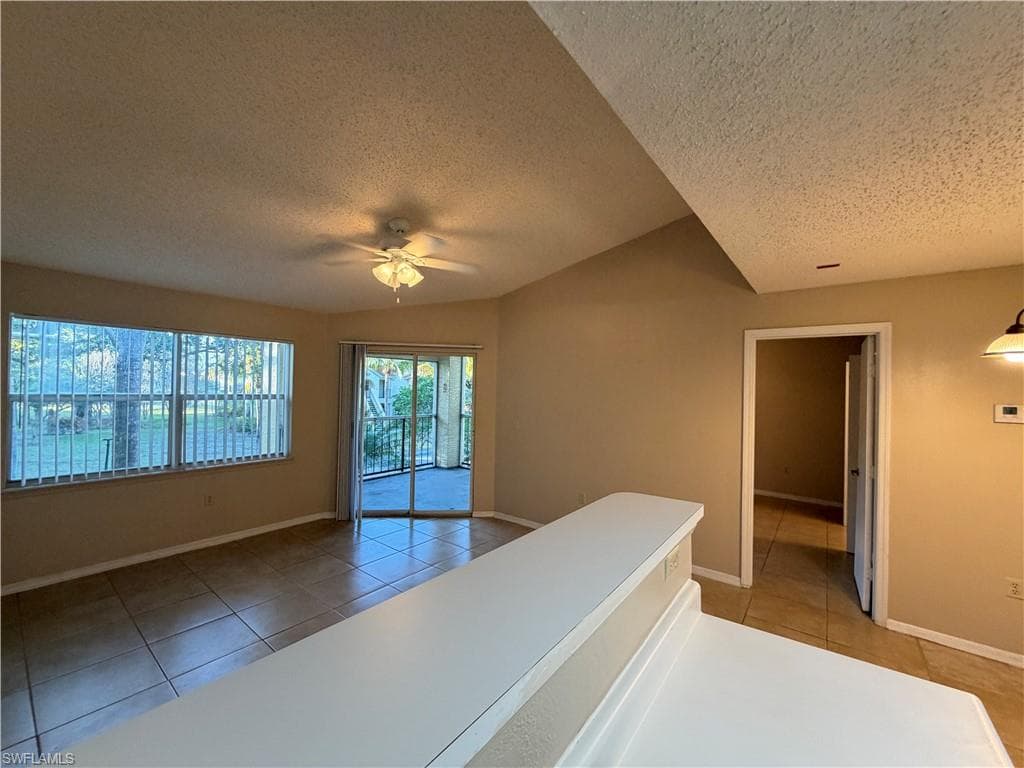 Spare room with a textured ceiling, light tile patterned floors, vaulted ceiling, and a ceiling fan