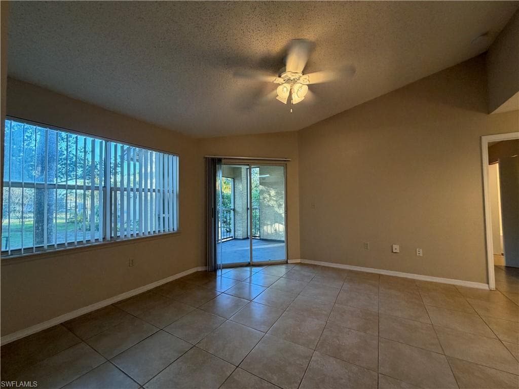 Tiled empty room with a textured ceiling, vaulted ceiling, and a ceiling fan