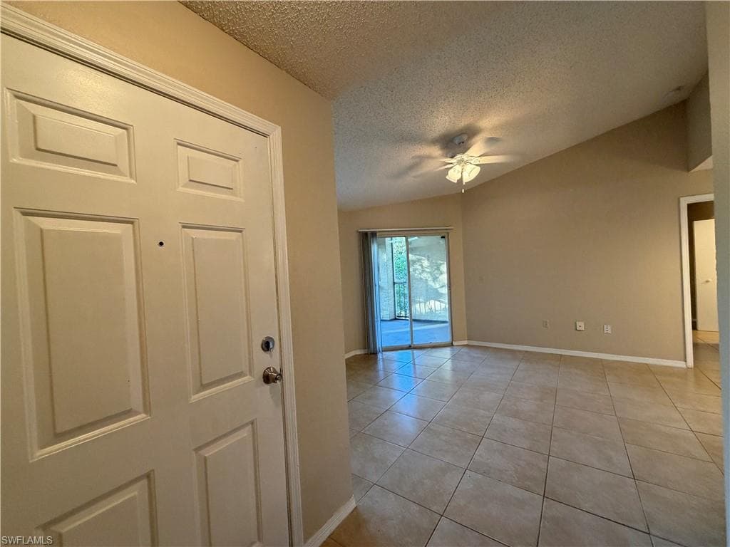 Unfurnished room with a textured ceiling, light tile patterned floors, a ceiling fan, and lofted ceiling
