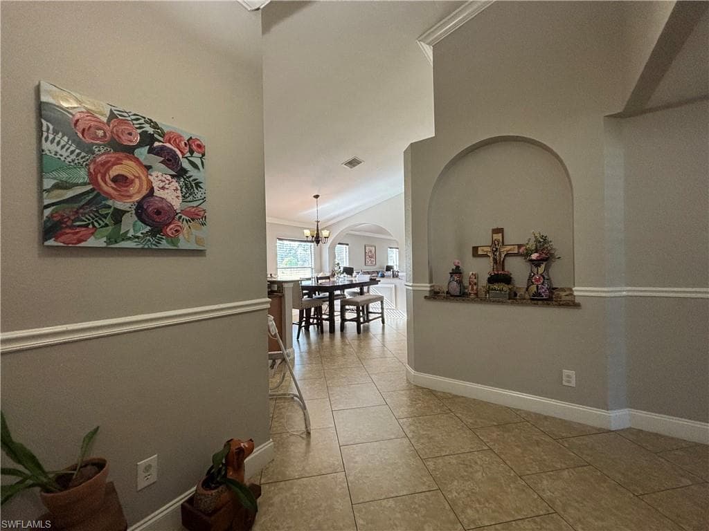 Corridor with arched walkways, high vaulted ceiling, crown molding, light tile patterned floors, and a chandelier