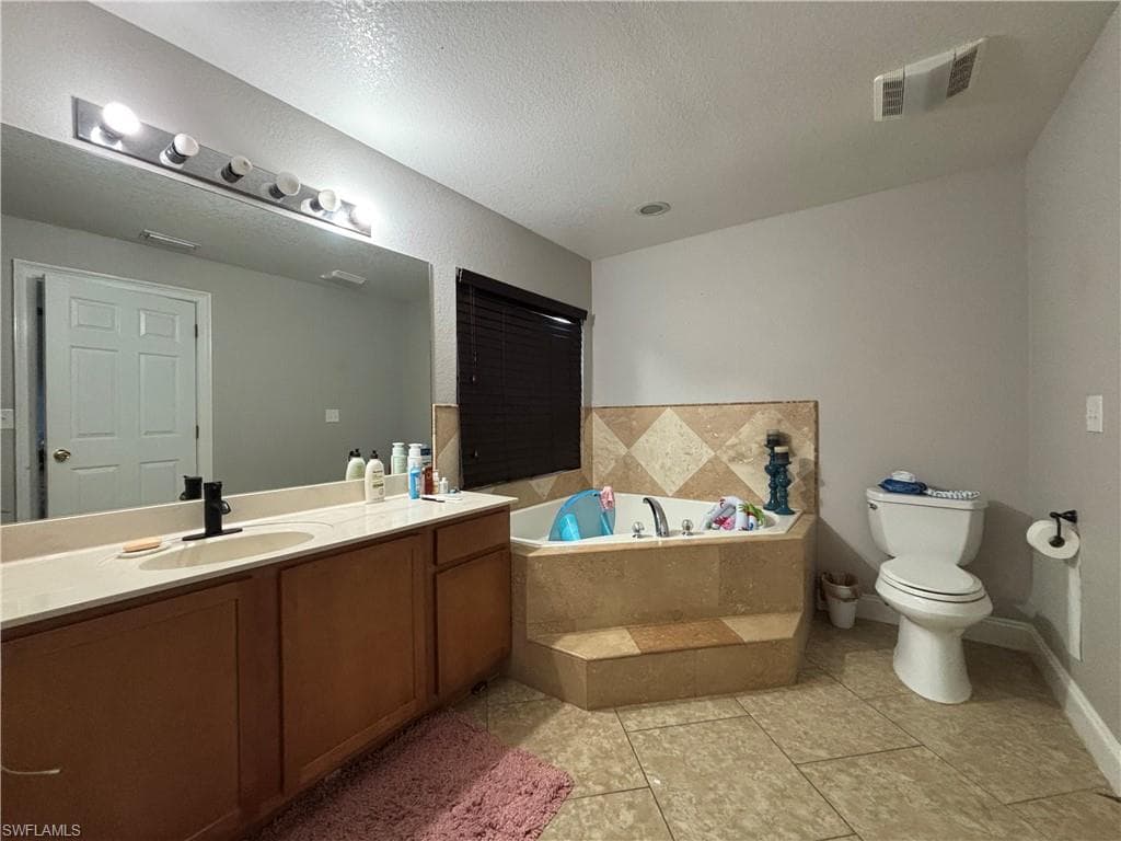 Bathroom with vanity, a garden tub, a textured ceiling, and light tile patterned floors