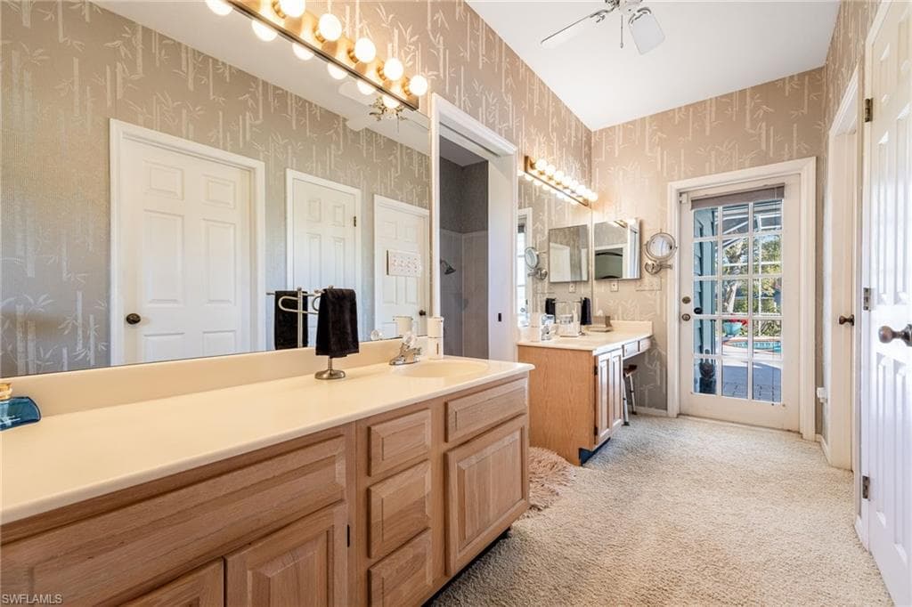 Bathroom featuring two vanities, light carpet, and a ceiling fan