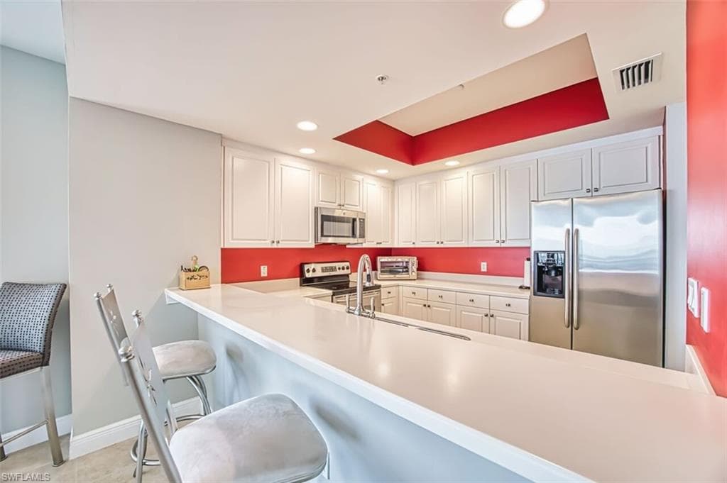 Kitchen featuring appliances with stainless steel finishes, a kitchen breakfast bar, light countertops, recessed lighting, and white cabinetry