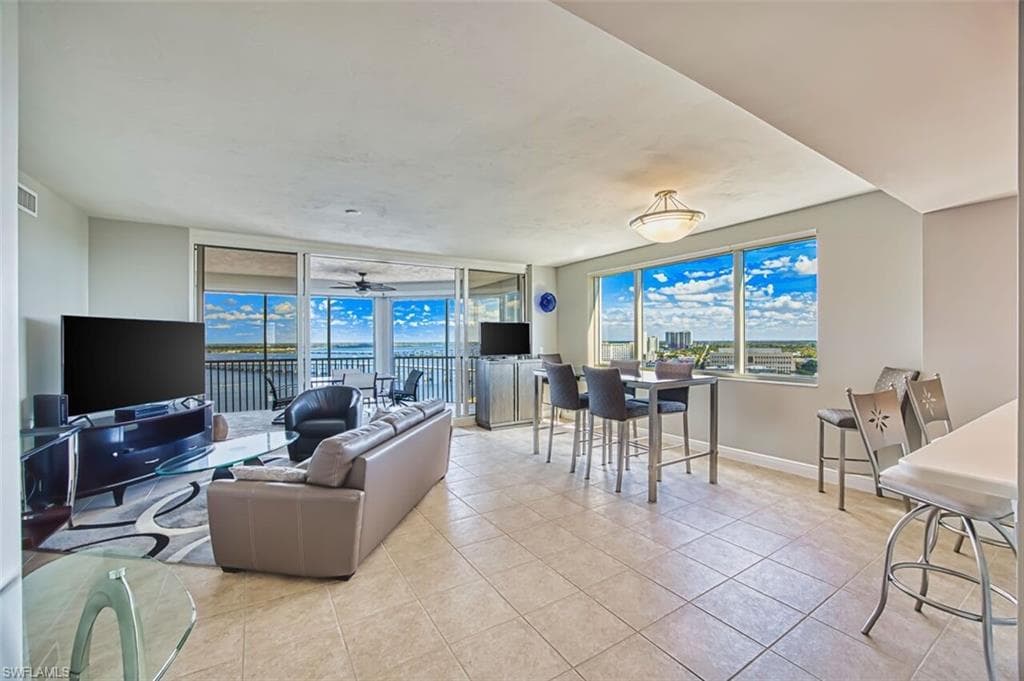 Living area with light tile patterned floors, expansive windows, and ceiling fan