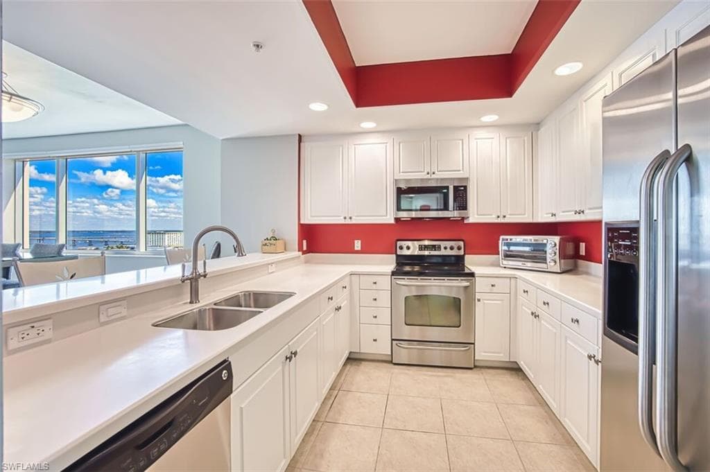 Kitchen with appliances with stainless steel finishes, recessed lighting, white cabinetry, and a tray ceiling