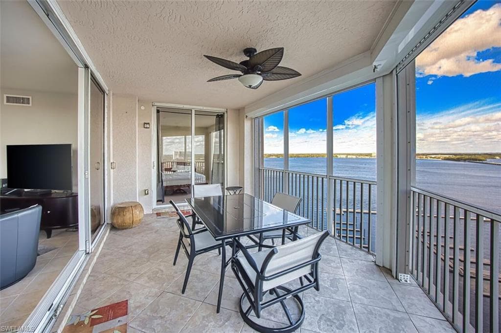 Sunroom with a ceiling fan, outdoor dining area, a water view, a textured ceiling, and tile patterned flooring