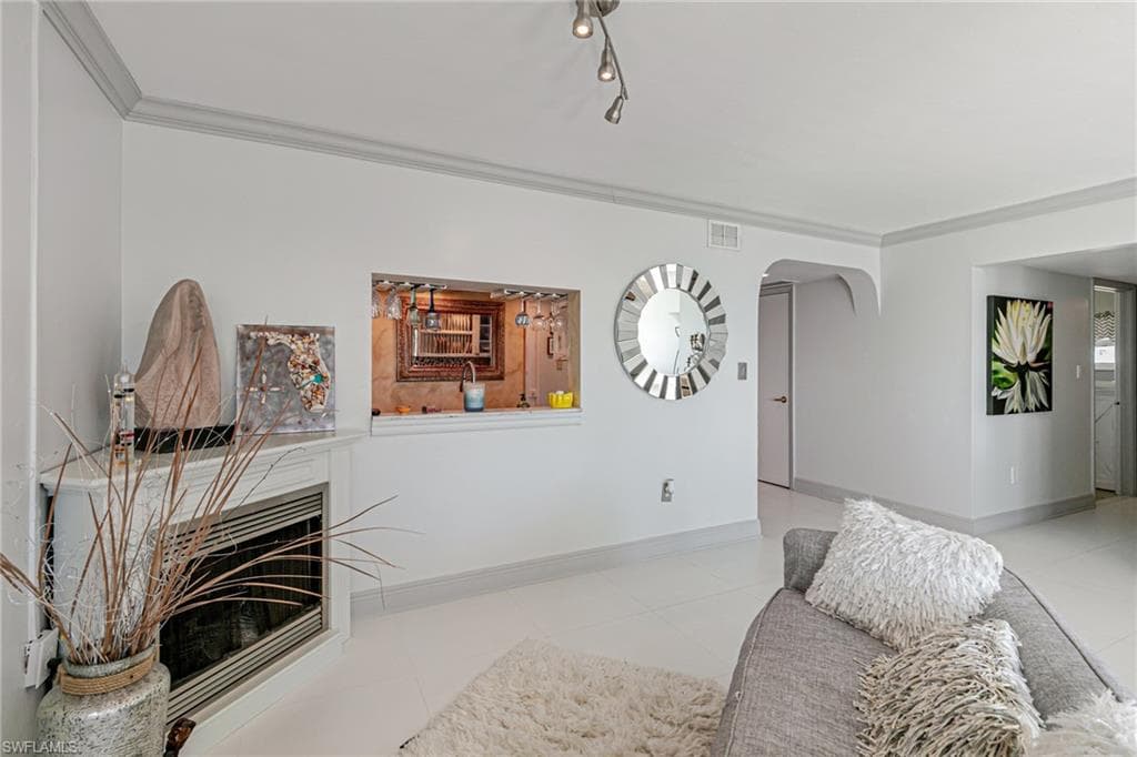Living area featuring ornamental molding, a fireplace, arched walkways, and light tile patterned flooring